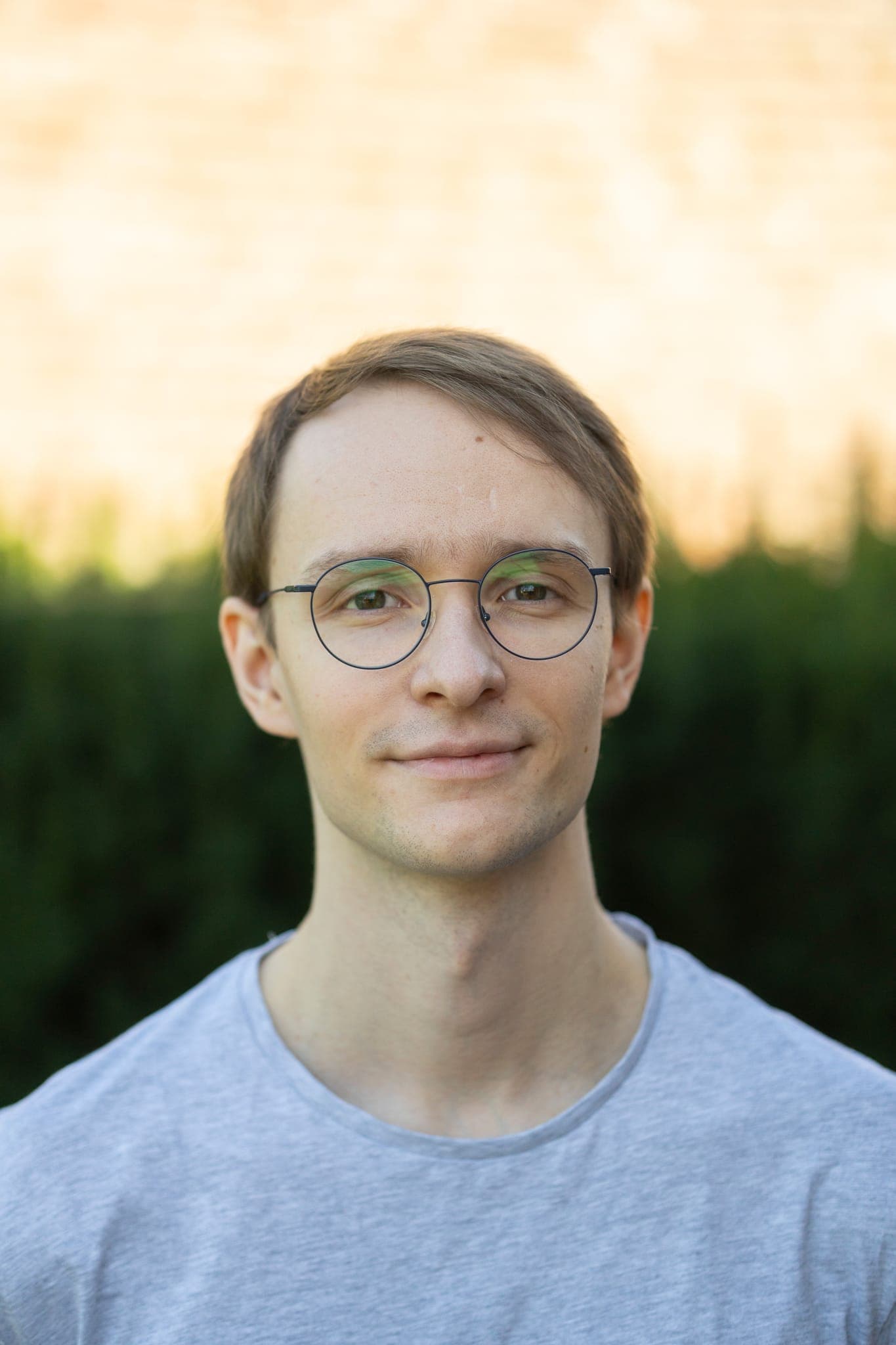 Florian Behne, frontales Porträt mit Brille vor einer Hecke im Abendlicht